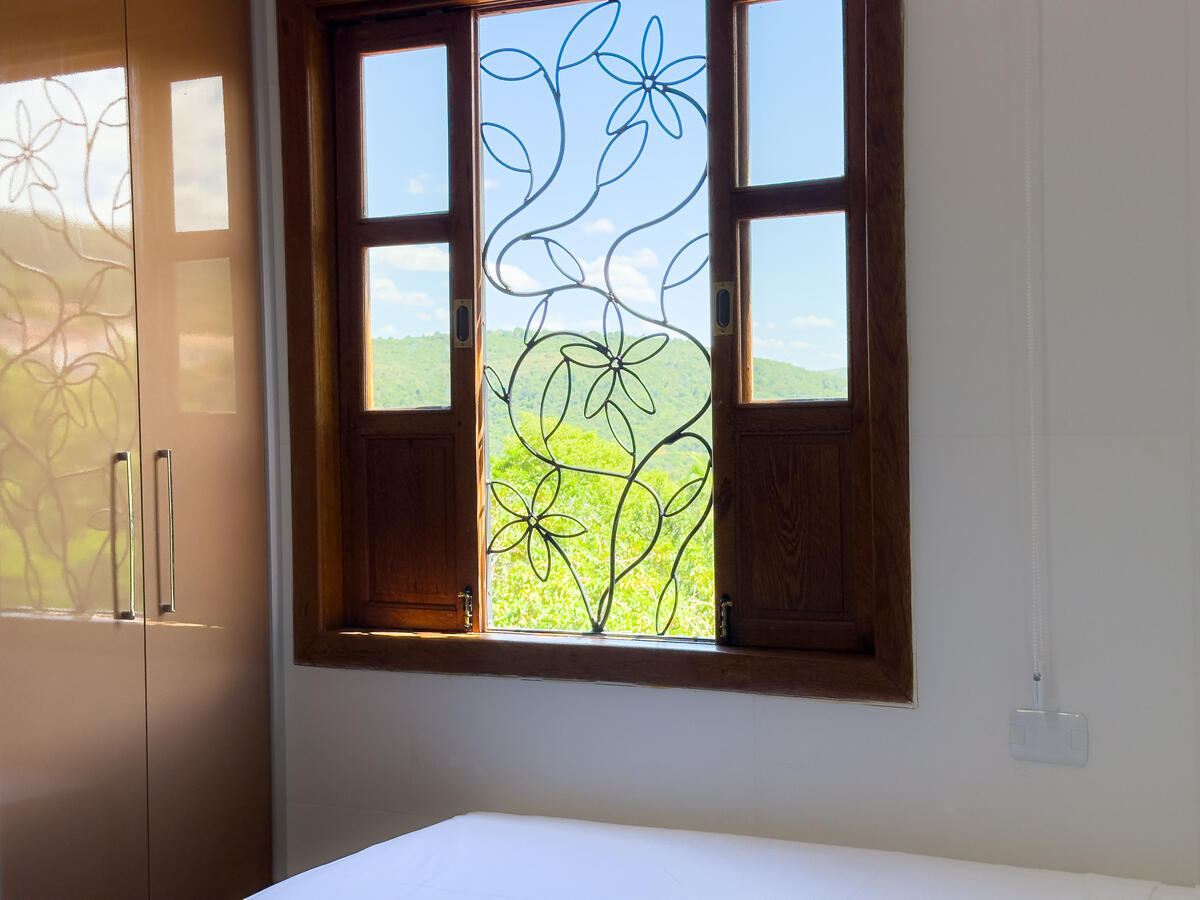 Janela de madeira do quarto com grade de ferro floral, aberta para a serra verde da Chapada