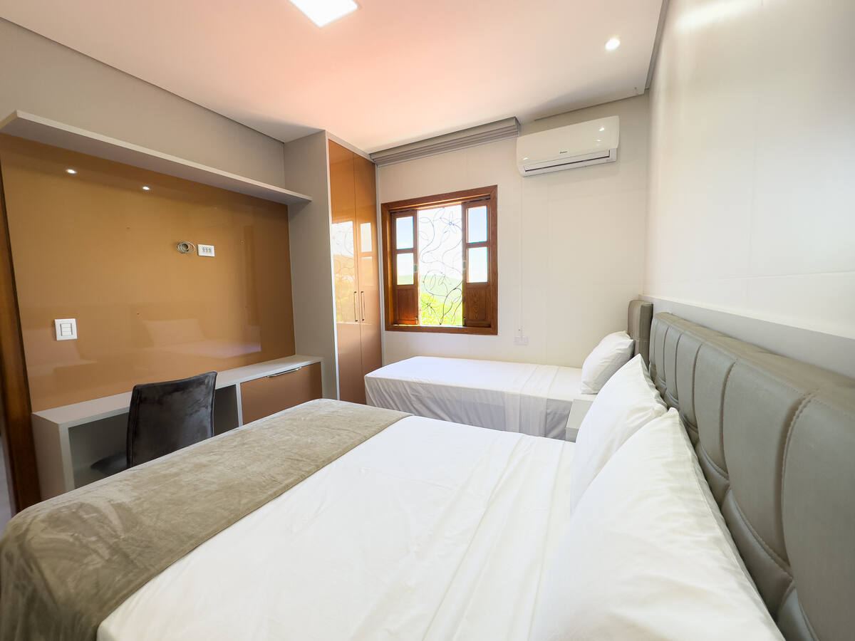 Quarto com cama de casal, cama de solteiro junto à janela e bancada