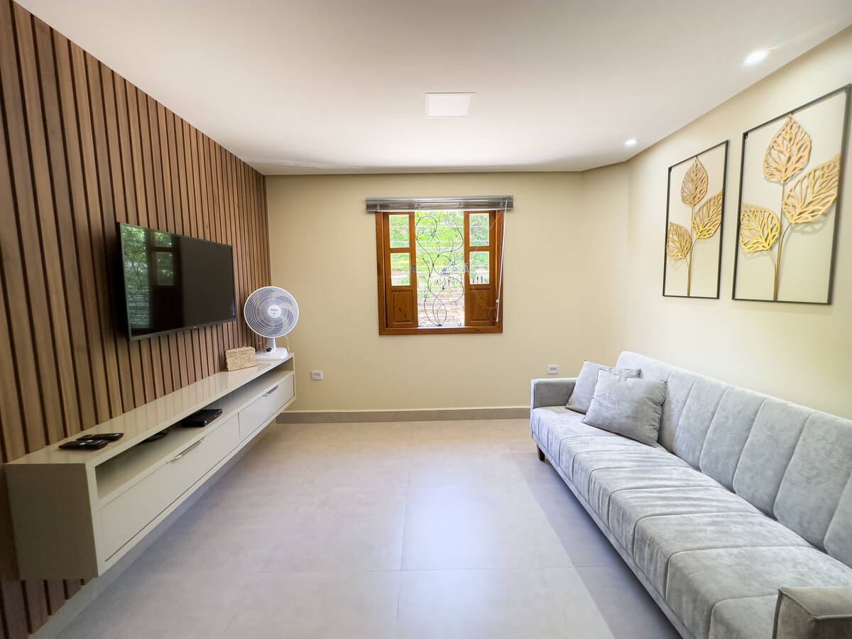 Sala com sofá amplo, TV e janela de madeira